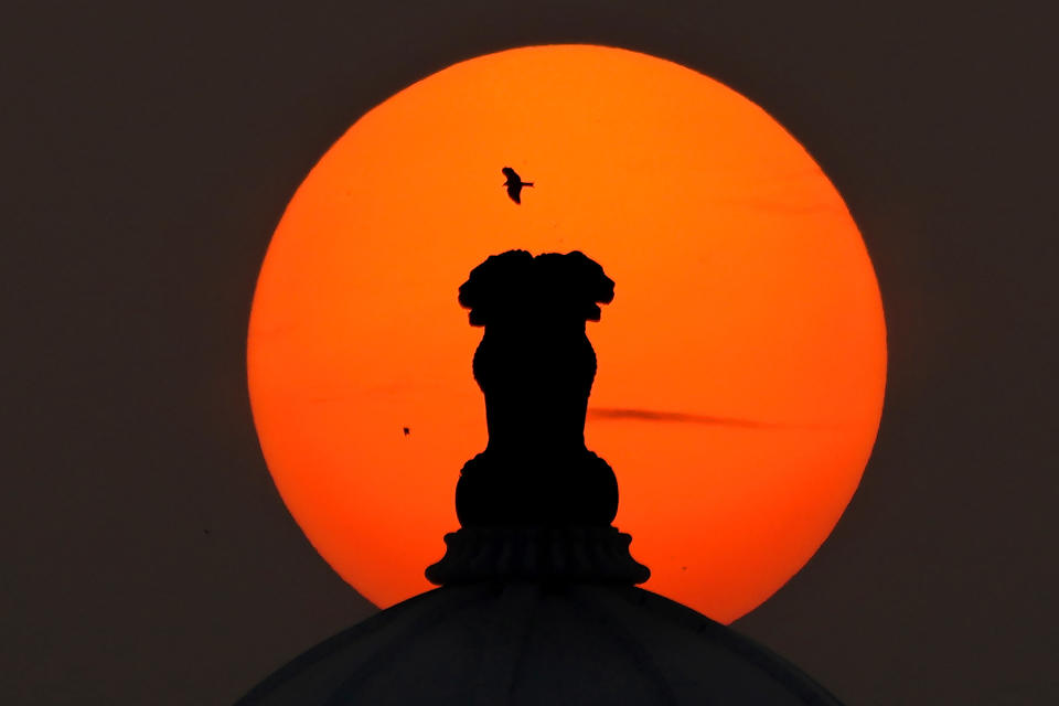 An eagle flies past an Indian emblem placed on the top of the Telangana State Secretariat building against the setting sun, in Hyderabad, India, Monday, Dec. 18, 2023. The emblem features four Asiatic lions standing back to back, symbolizing power, courage, confidence and faith. (AP Photo/Mahesh Kumar A.)