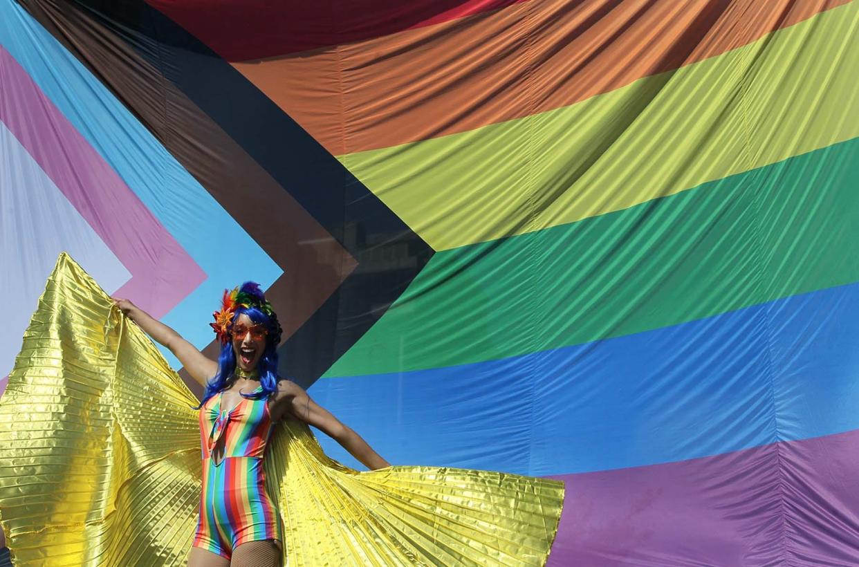 Tasha Walls, standing on stilts, with the group from Baxter's Speakeasy, stands in front of the gigantic Progress Pride flag as she poses with groups for photos Saturday.