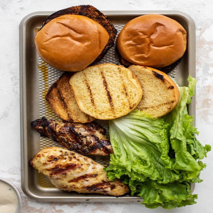 Ingredients for grilled chicken Caesar sandwiches on a sheet pan.