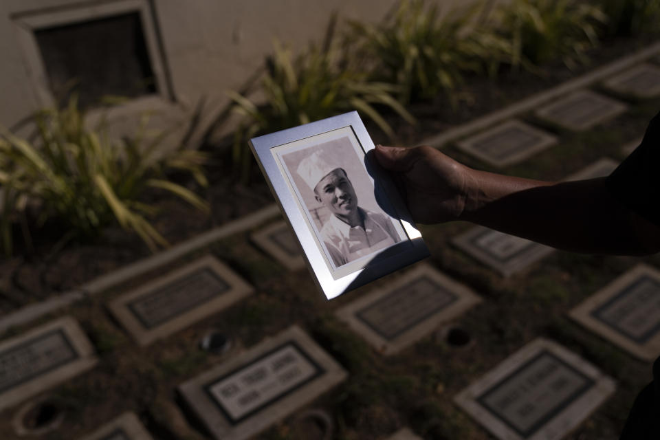 Holding a photo of his grandfather, Giichi Matsumura, Clyde Matsumura pauses while visiting his father's grave after a memorial service for his grandfather at Woodlawn Cemetery in Santa Monica, Calif., Monday, Dec. 21, 2020. Giichi Matsumura, who died in the Sierra Nevada on a fishing trip while he was at the Japanese internment camp at Manzanar, was reburied in the same plot with his wife 75 years later after his remains were unearthed from a mountainside grave. (AP Photo/Jae C. Hong)