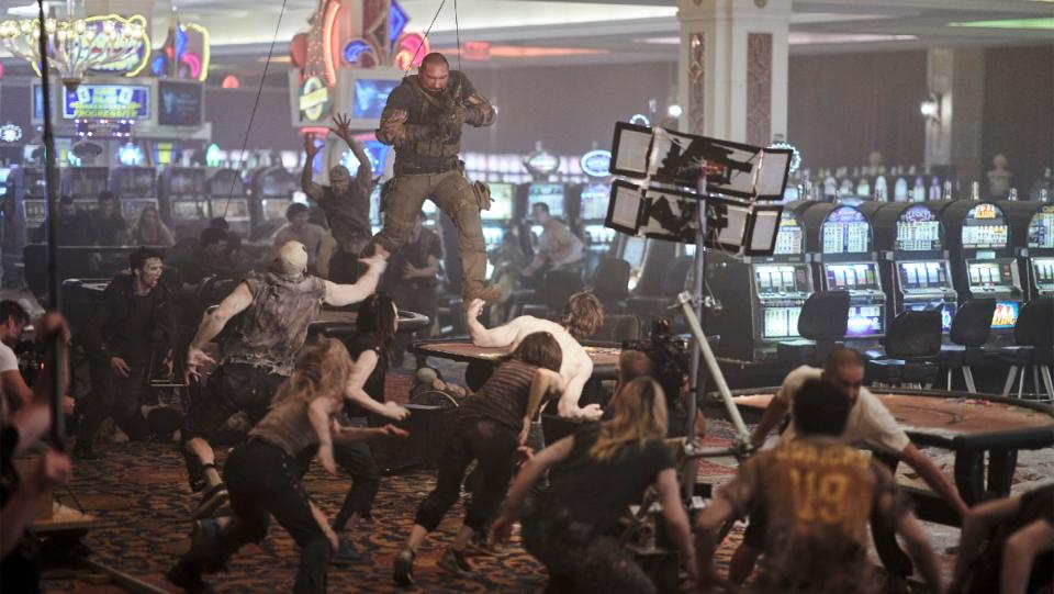 Dave Bautista hangs from wires above a group of zombies during a stunt in a behind-the-scenes still from Army of the Dead.