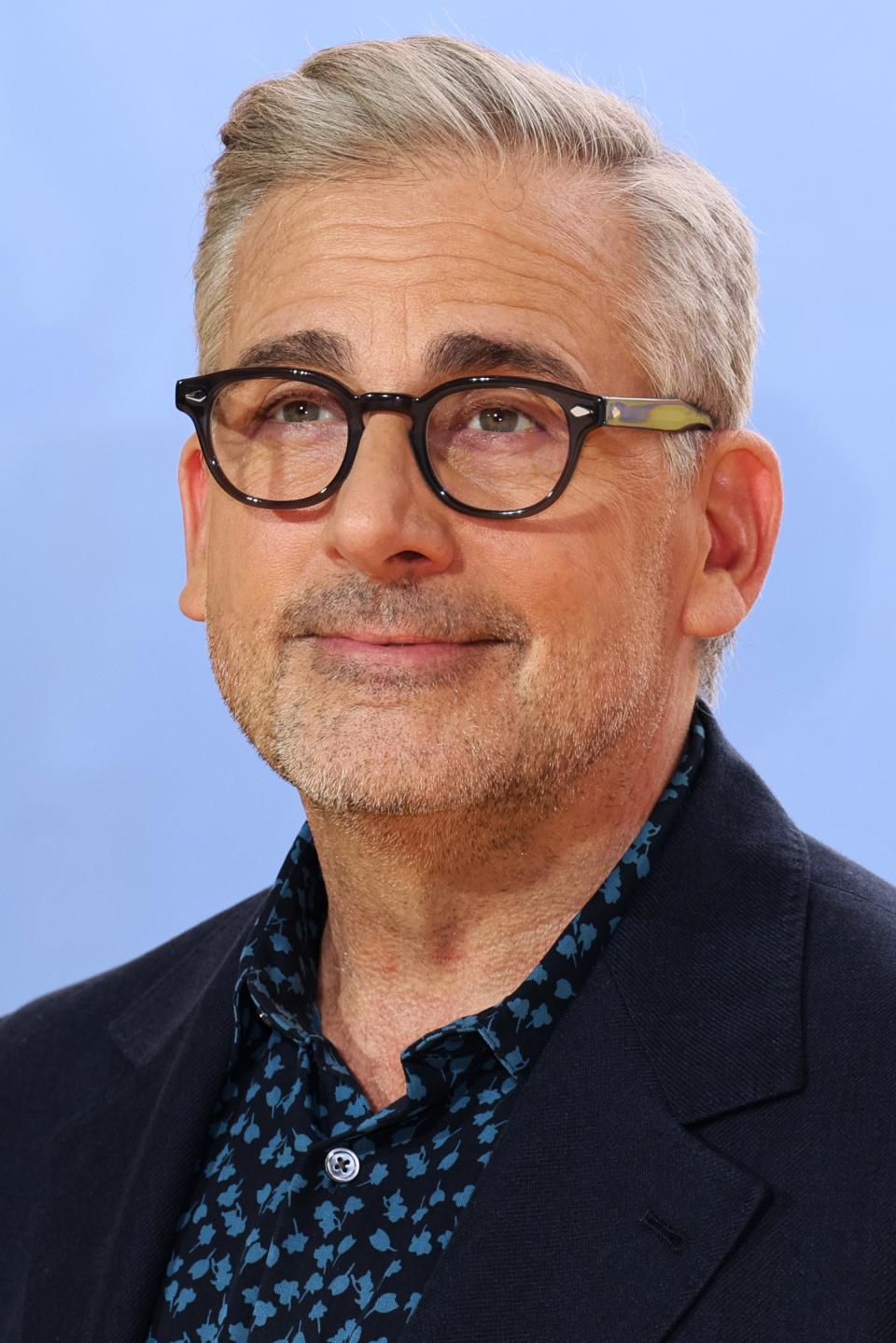 Steve Carell smiling, wearing glasses, a dark blazer, and a patterned shirt at the 
