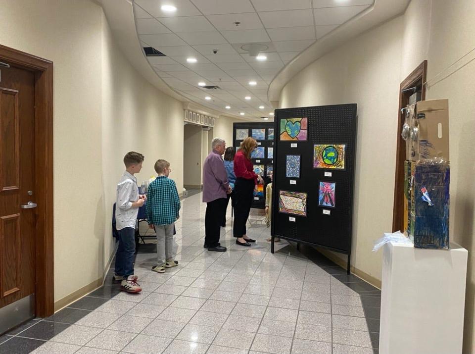 Lizzie Emmons, executive director of the Jackson Arts Council, (in red), and Andrew Boks, chair of Public Art Commission, (in purple), are led by a young contestant to look at her displayed artwork in City Hall.