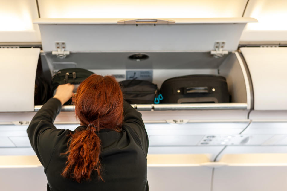 A woman loading luggage in an overhead bin