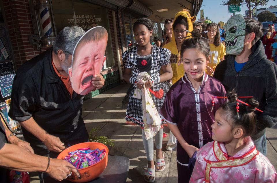 Randy Zaragoza owner of Zaragoza's Cal-Pine on the Ave, left, wears a giant baby mask as he hands out candy on Pacific Avenue along the Miracle Mile during the annual Trick or Treat on the Mile Halloween event in Stockton.  [CLIFFORD OTO/THE RECORD]