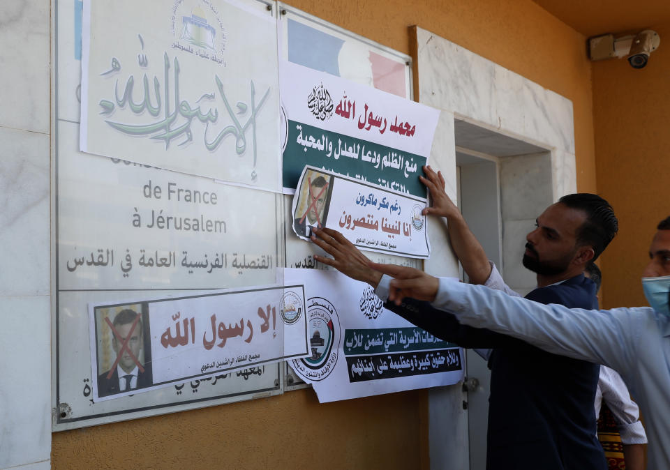 An Islamic scholar posts defaced pictures of French President Emmanuel Macron at the entrance of the French Cultural center during a protest against the publishing of caricatures of the Prophet Muhammad they deem blasphemous, in Gaza City, Monday, Oct. 26, 2020. Arabic reads: "Despite Macron's malice, we rise up to our Prophet" and referring to criticism, "Anything but God's messenger." (AP Photo/Adel Hana)