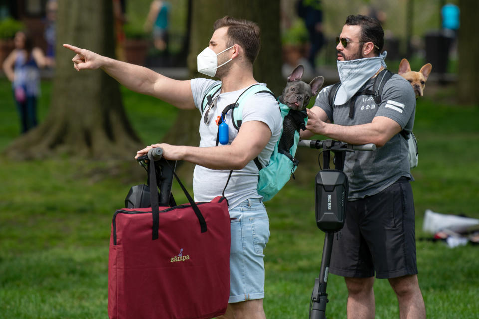 Two people wearing masks carry their dogs in their backpack through Sheep Meadow, Central Park as temperatures rose amid the coronavirus pandemic on May 2, 2020 in New York City. (Photo: Alexi Rosenfeld/Getty Images)