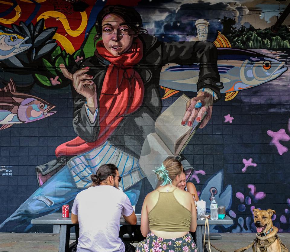 People enyoy a snack at East Lansing Arts Festival in 2021 infront of a new mural painted by a collaboration or Michigan State students, former students and faculty.