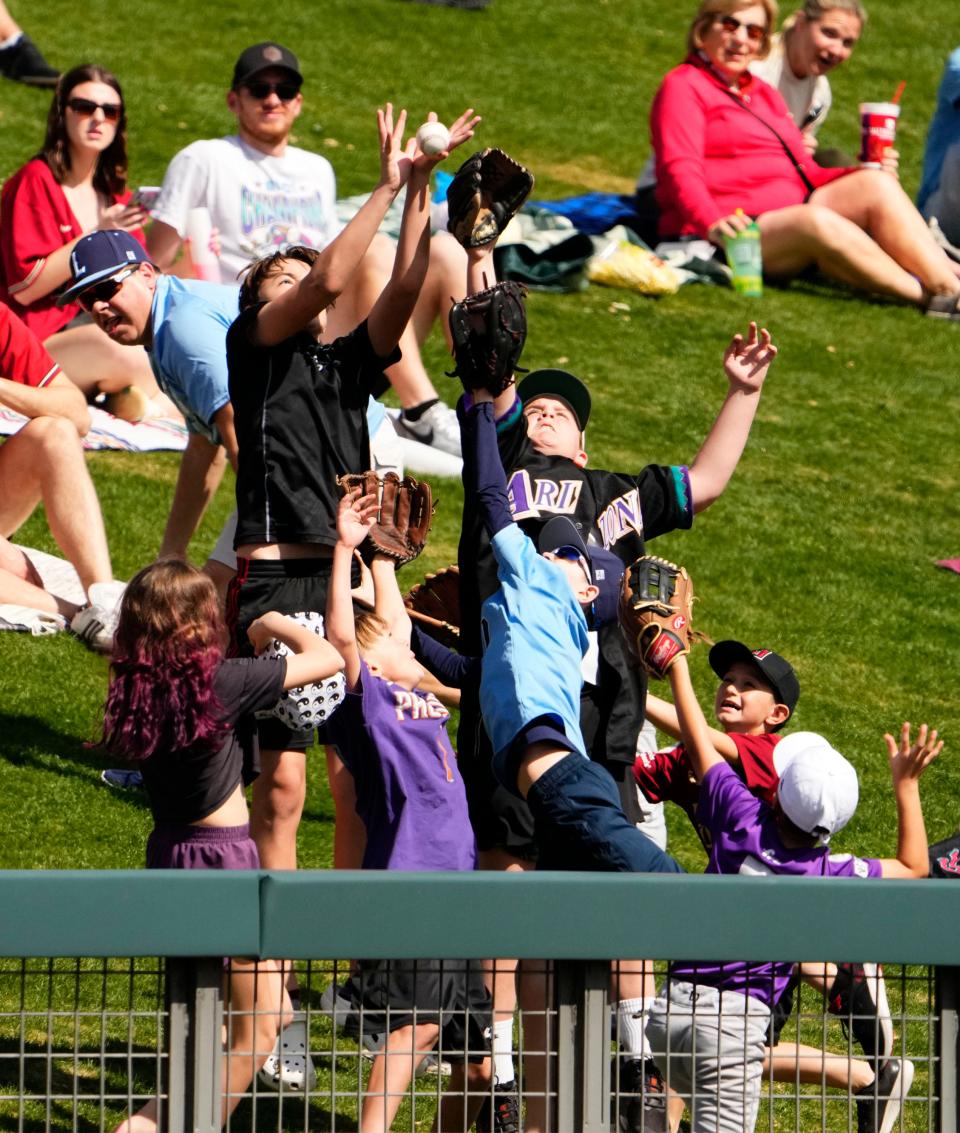 Fans try to catch a baseball thrown to them from Arizona Diamondbacks left fielder Lourdes Gurriel Jr. (12) in the second inning during a spring training game against the Texas Rangers at Salt River Fields in Scottsdale on March 8, 2023.