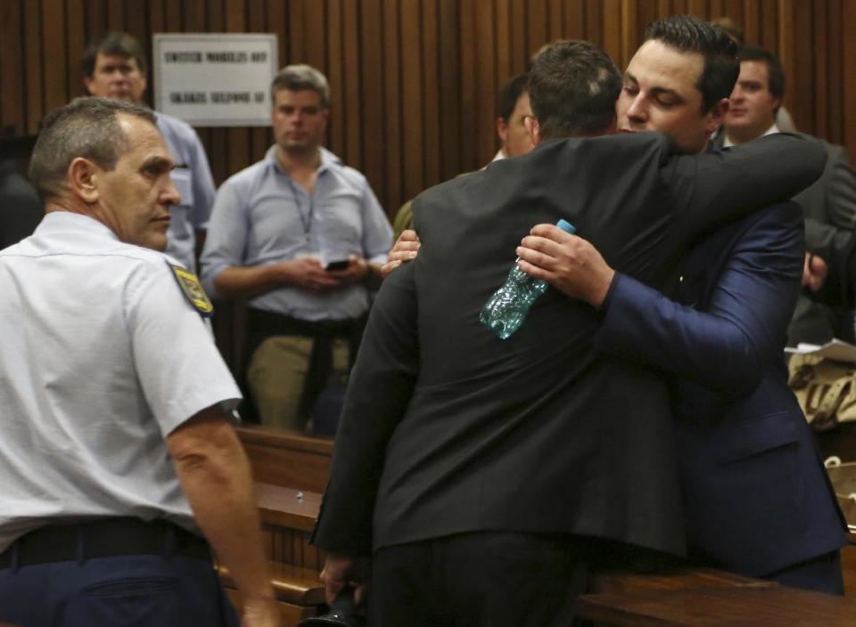 Carl Pistorius, right, embraces his brother Oscar as the police officer watches at the end the court session for his trial at the high court in Pretoria, South Africa, Monday, March 3, 2014. Pistorius is charged with murder for the shooting death of his girlfriend, Reeva Steenkamp, on Valentines Day in 2013. (AP Photo/Themba Hadebe, Pool)