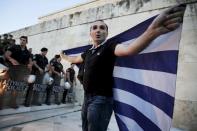 An anti-EU protester unfurls a Greek national flag next to riot police guarding the steps in front of the parliament building during a demonstration of about five hundred people in Athens, Greece July 13, 2015. REUTERS/Jean-Paul Pelissier