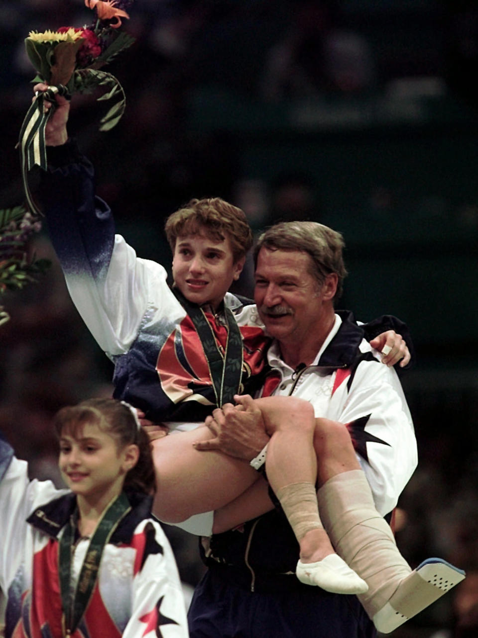 FILE - In this July 23, 1996, file photo, U.S. gymnastics coach Bela Karolyi carries injured Kerri Strug following the awarding ceremony at the women's team gymnastics competition at the Centennial Summer Olympic Games in Atlanta. The U.S. won the gold. At left is Dominique Moceanu. (AP Photo/Susan Ragan, File)