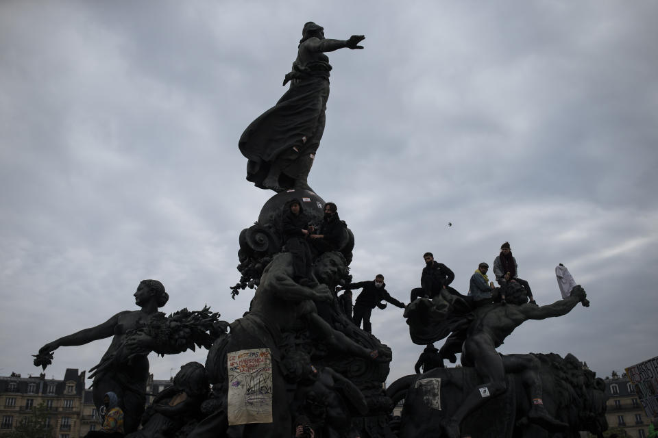 Protesters are silhouetted as they clamber over the Place de la Nation statue during May Day march, Saturday, May 1, 2021 in Paris. Protesters, workers and union leaders demonstrated during slimmed down but still boisterous May Day marches on Saturday, demanding more labor protections amid the coronavirus pandemic.(AP Photo/Lewis Joly)