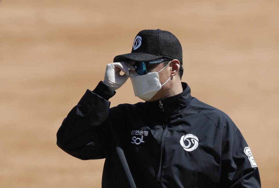 First base umpire Lee Gye-sung wearing a mask and gloves as a precaution against the new coronavirus adjusts glasses during the pre-season baseball game between Doosan Bears and LG Twins in Seoul, South Korea, Tuesday, April 21, 2020. South Korea's professional baseball league has decided to begin its new season on May 5, initially without fans, following a postponement over the coronavirus. (AP Photo/Lee Jin-man)