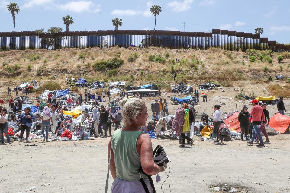 A woman looks out toward hundreds of migrants who have amassed at the border fence near Monument Rd. close to the International Wastewater Treatment Plant in San Diego, Calif., May 11, 2023. 
