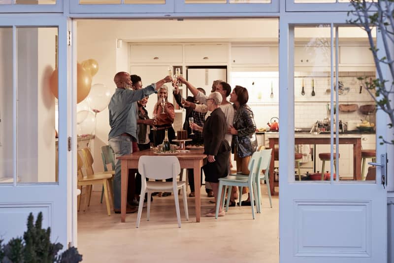 Cheerful male and female toasting drinks during birthday party in house