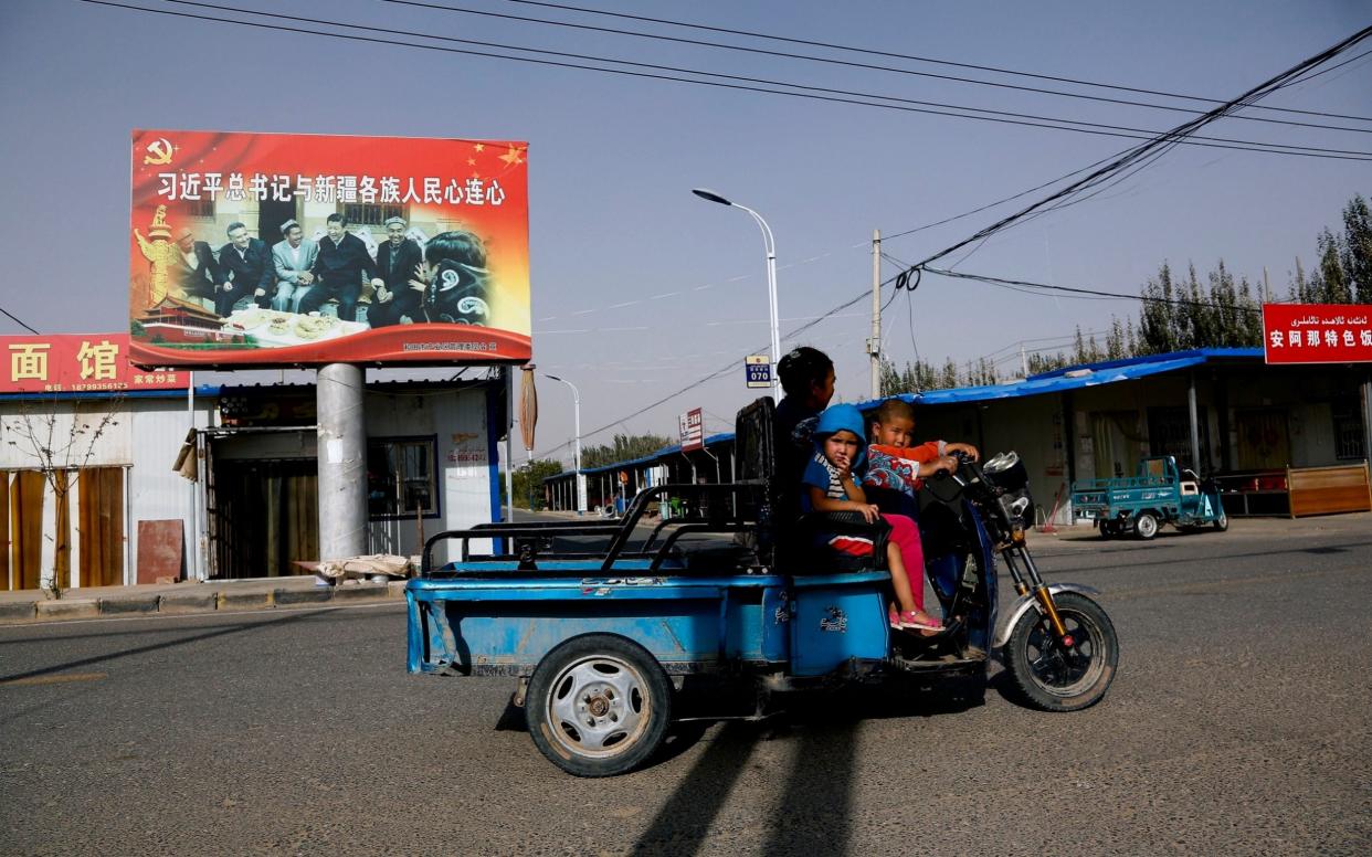 A Uighur woman and children ride past a propaganda poster showing China's President Xi Jinping joining hands with Uighur elders Xinjiang region - AP