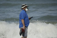 A man wears a mask to help prevent the spread of the coronavirus as he walks alone on the beach Sunday, May 31, 2020, at Satellite Beach, Fla. (AP Photo/Charlie Riedel)