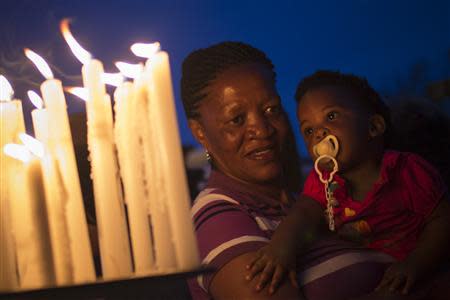 A woman holds a child near a candlelight memorial outside the Nelson Mandela house in the Houghton Estates neighbourhood of Johannesburg, December 7, 2013. REUTERS/Adrees Latif