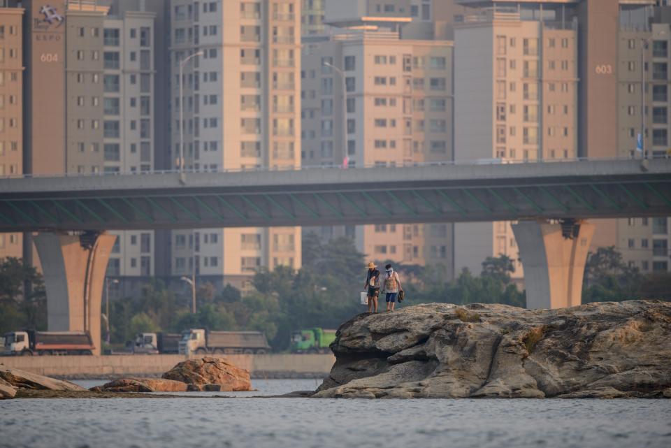 A couple walk along rocks before the apartment blocks and the skyline of the Songdo area of Incheon on September 25, 2014. Incheon is hosting the 2014 Asian Games. AFP PHOTO / Ed Jones (RILEY JONES/AFP via Getty Images)