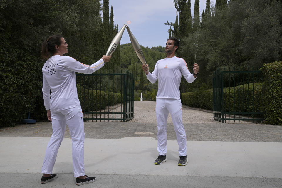 The first torch bearer, Greek olympic gold medalist Stefanos Douskos, right, passes the flame to first French torchbearer, three-time Olympic medallist Laure Manaudou, near the monument to Pierre de Coubertin, in the background, after the official ceremony of the flame lighting for the Paris Olympics, at the Ancient Olympia site, Greece, Tuesday, April 16, 2024. The flame will be carried through Greece for 11 days before being handed over to Paris organizers on April 26. (AP Photo/Thanassis Stavrakis)