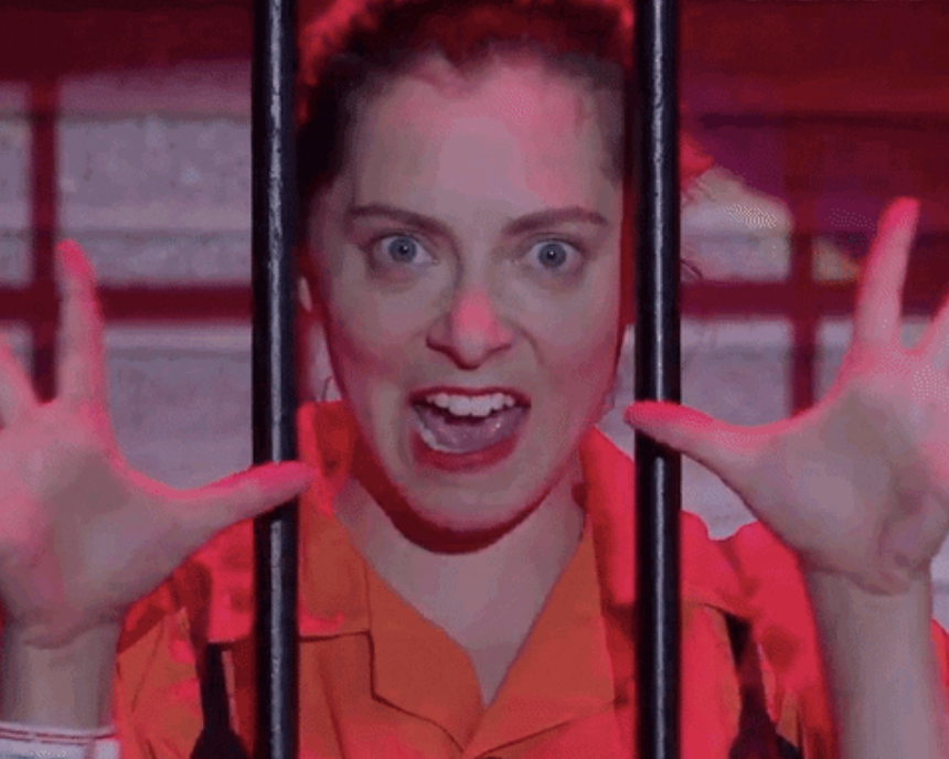 A woman behind bars with her hands up, like she's singing a song and doing jazz hands