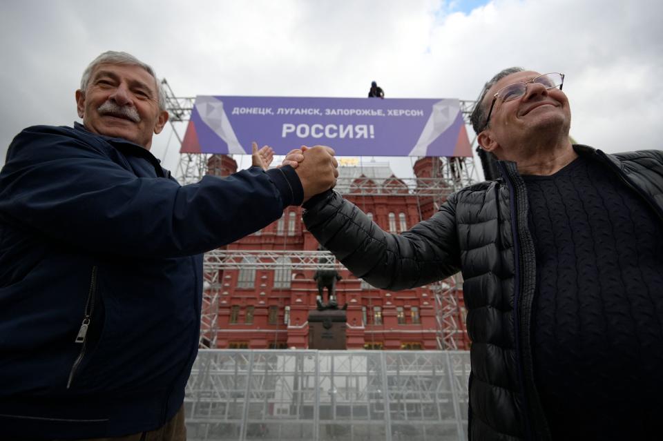 Two men celebrate annexation move by Russia in front of the stage where a formal ceremony will be held today. Russia will formally annex four regions of Ukraine its troops occupy at a grand ceremony in Moscow, the Kremlin has announced (AFP via Getty Images)