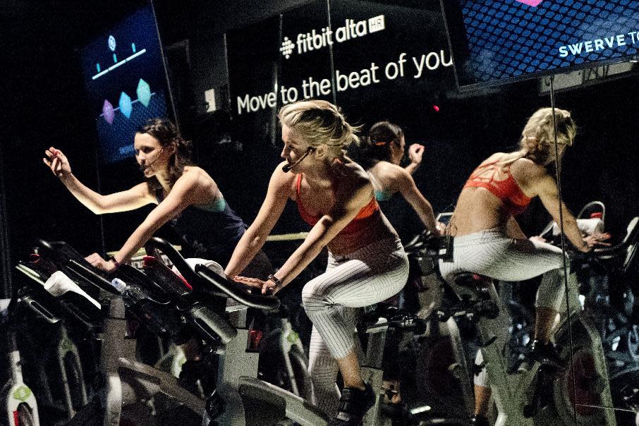 In this March 1, 2017 photo, Jamey Powell, left, and Julianne Hough lead an exercise class as the participants are introduced to the Alta HR fitness tracker at Swerve cycling center in New York. Fitbit is the leading seller of wearable devices, but it’s facing a steep decline because most of its sales are in the U.S., where many people who want a fitness tracker already have one. (AP Photo/Mark Lennihan)