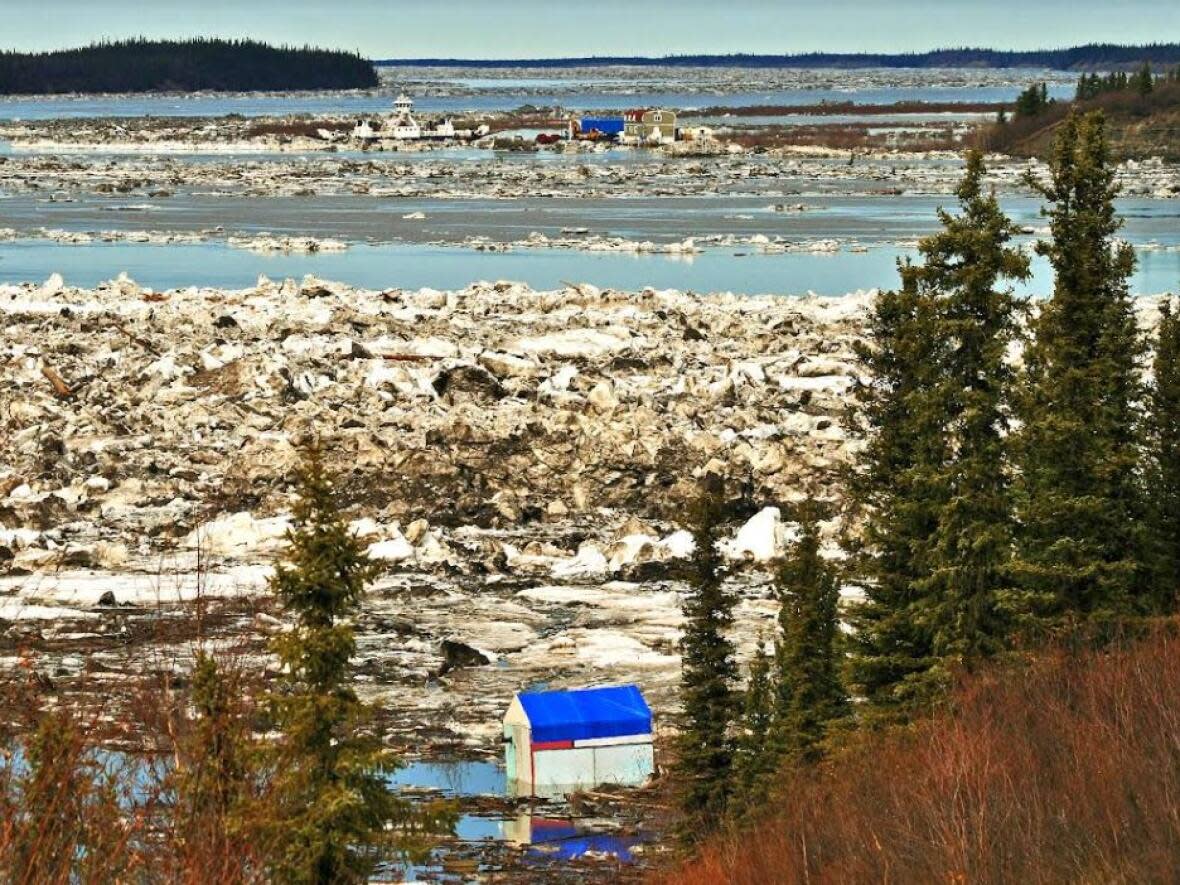 A photo looking north from the gravel quarry in Tsiigehtchic shows a flooded tent frame in the foreground, and the MV Louis Cardinal ferry in the distance. (Submitted by Lawrence Norbert - image credit)