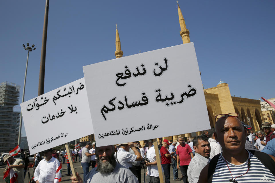 In this Tuesday, July 16, 2019 photo, retired Lebanese soldiers hold Arabic placards that read: "Will not pay your corruption taxes," right, and "your tax is extortion without services," as they protest near the parliament building where lawmakers and ministers are discussing the draft 2019 state budget, in Beirut, Lebanon. As the economic crisis deepens in Lebanon, so has the public’s distrust in the ability of the old political class, widely viewed as corrupt and steeped in personal rivalries, to tackle major reform. Many fear a Greek-style bankruptcy, without the European Union to fall back on, and with a potentially more violent social unrest in the small country wedged between war-torn Syria and Israel. (AP Photo/Hussein Malla)