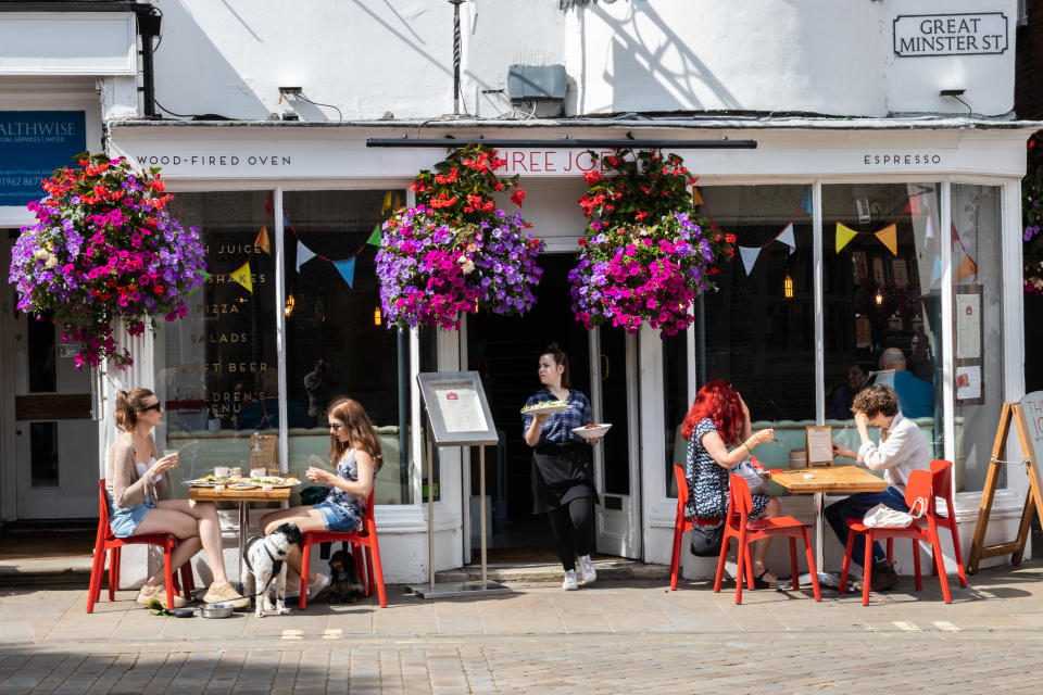 living wage cost of living crisis Winchester, Hampshire, UK the front of a cafe with people sitting at tables in the sun enjoying food and a coffee with a waitress carrying