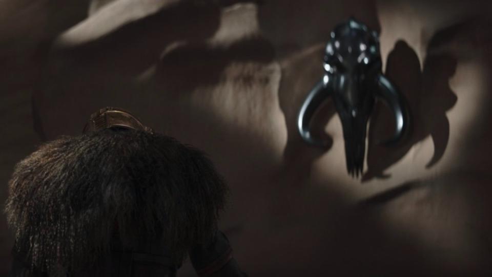 The back of the Armorer in her forge cave with a mythosaur skull behind her on the wall on The Mandalorian