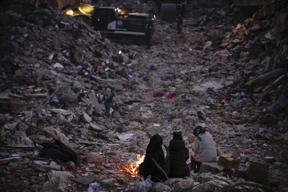 Members of a family keep warm next to a fire as they follow a rescue team searching for their relatives among destroyed building in Antakya, southern Turkey, Wednesday, Feb. 15, 2023. Ever since the powerful 7.8 earthquake that has become Turkey's deadliest disaster in modern history, survivors have been gathering outside destroyed buildings, refusing to leave. (AP Photo/Francisco Seco)