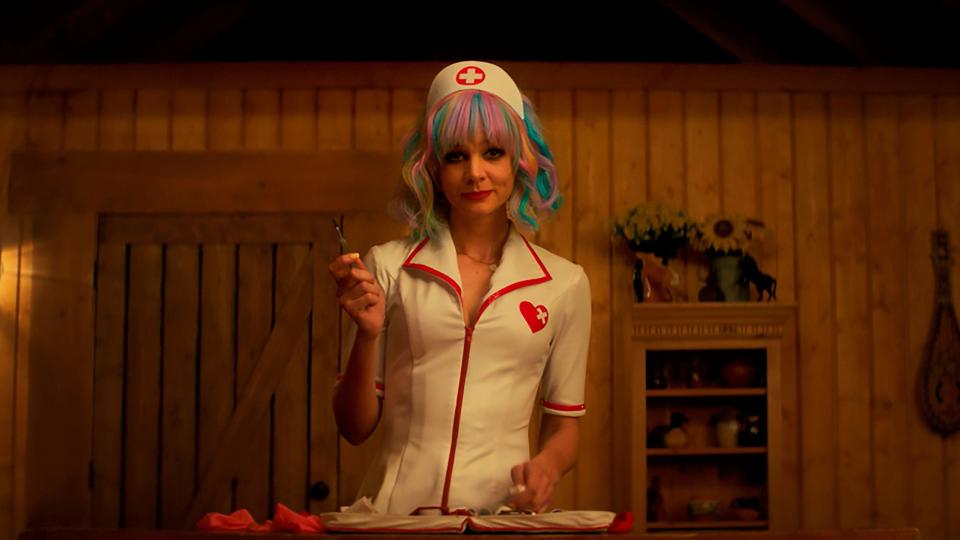 A woman with colorful hair in a latex nurse outfit wields a scalpel ominously