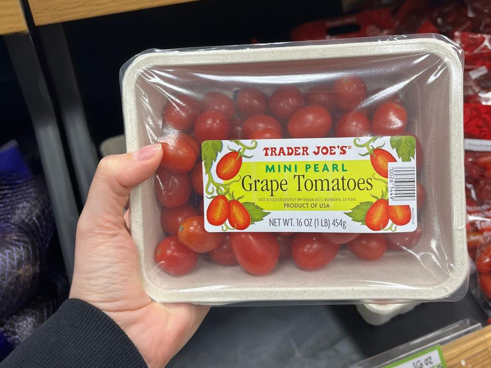 hand holding up a carton of mini pearl grape tomatoes at trader joes