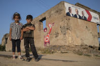 Armenian children look at a photographer standing in front of a damaged building with the posters of parties candidates in Shurnkh village, about 200 km. (125 miles) south-east of Yerevan, Armenia, Tuesday, June 15, 2021. The village was cut in two by a newly defined border with Azerbaijan, and she lost her house in the peace deal. (AP Photo/Areg Balayan)