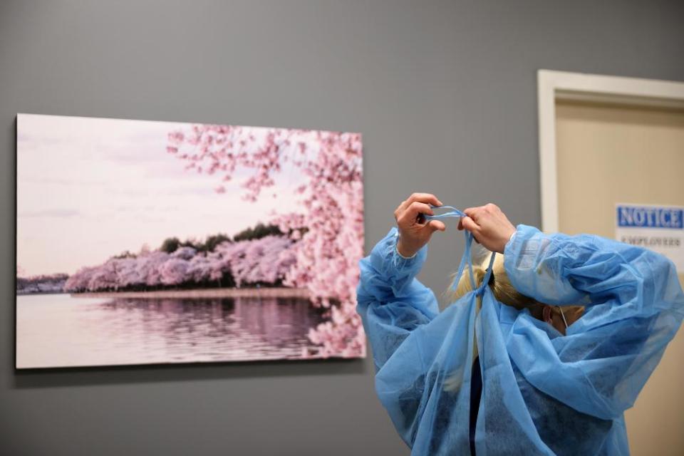 A healthcare workers puts on a sterile gown while helping test patients for coronavirus in Virginia.