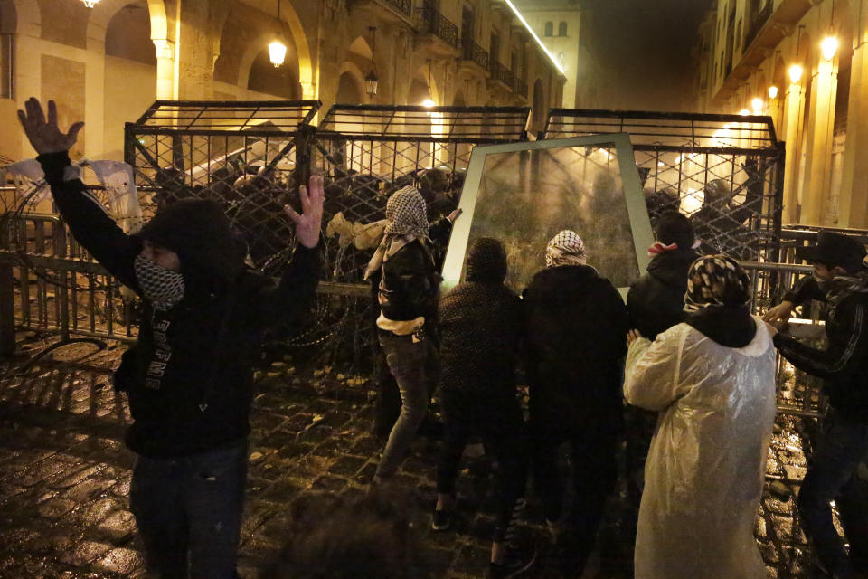 Anti-government protesters throw a glass panel against the riot police who are standing behind barriers defense, during ongoing protests against the political elites who have ruled the country for decades, in Beirut, Lebanon, Sunday, Jan. 19, 2020. Lebanese security forces used tear gas, water cannons and rubber bullets in clashes with hundreds of anti-government protesters outside the country's Parliament on Sunday, as violence continued to escalate in a week of rioting in the capital. (AP Photo/Hassan Ammar)