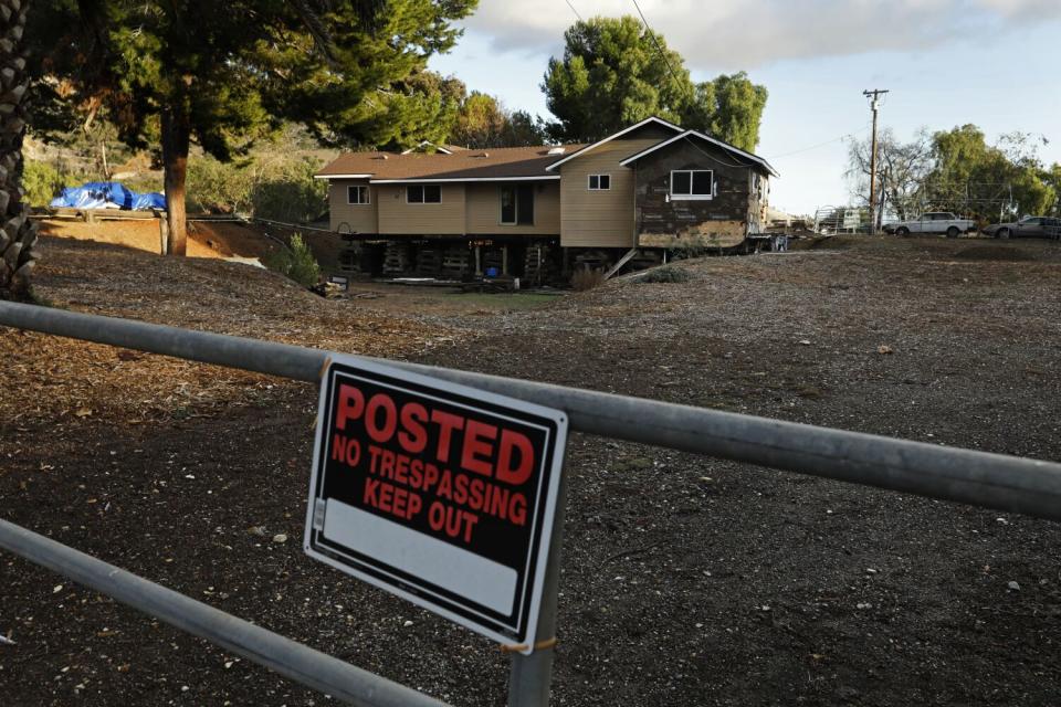 A house propped up on timber cribbing behind a No Trespassing sign.