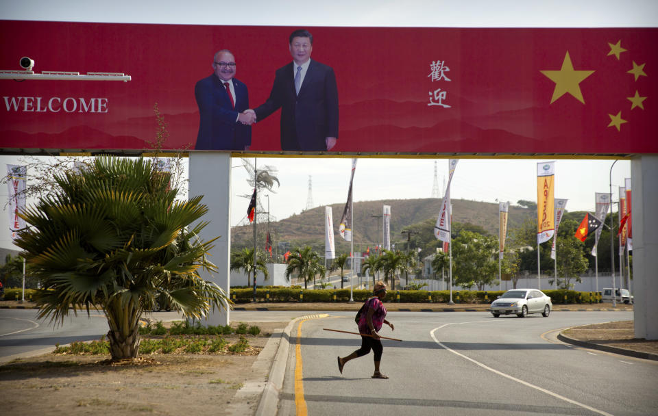 In this Nov. 15, 2018, photo, a woman crosses the street near a billboard commemorating the state visit of Chinese President Xi Jinping in Port Moresby, Papua New Guinea. As world leaders arrive in Papua New Guinea for a Pacific Rim summit, the welcome mat is especially big for China’s President Xi Jinping. With both actions and words, Xi has a compelling message for the South Pacific’s fragile island states, long both propped up and pushed around by U.S. ally Australia: they now have a choice of benefactors. (AP Photo/Mark Schiefelbein)