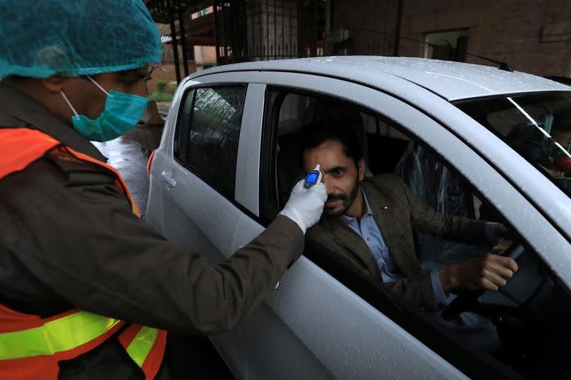 A rescue worker wears protective hand gloves as he checks a man?s temperature amid coronavirus fears, at the entrance of the government office building in Peshawar
