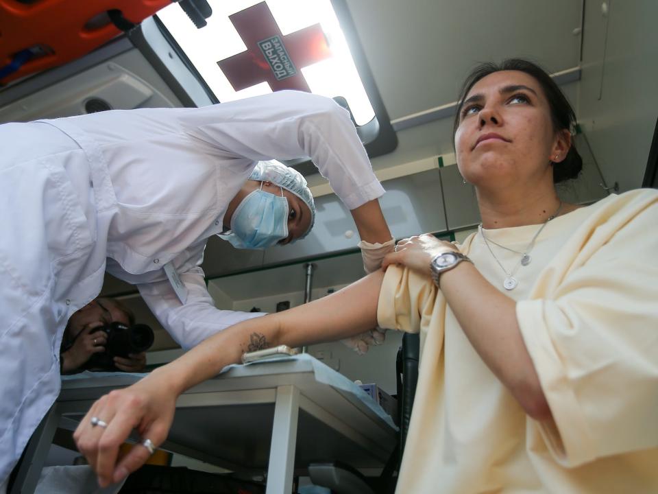 A health worker wearing protective equipment is administering a Sputnik V COVID vaccine to a young woman in a ambulance, pn May 29 in Tatarstan, Russian