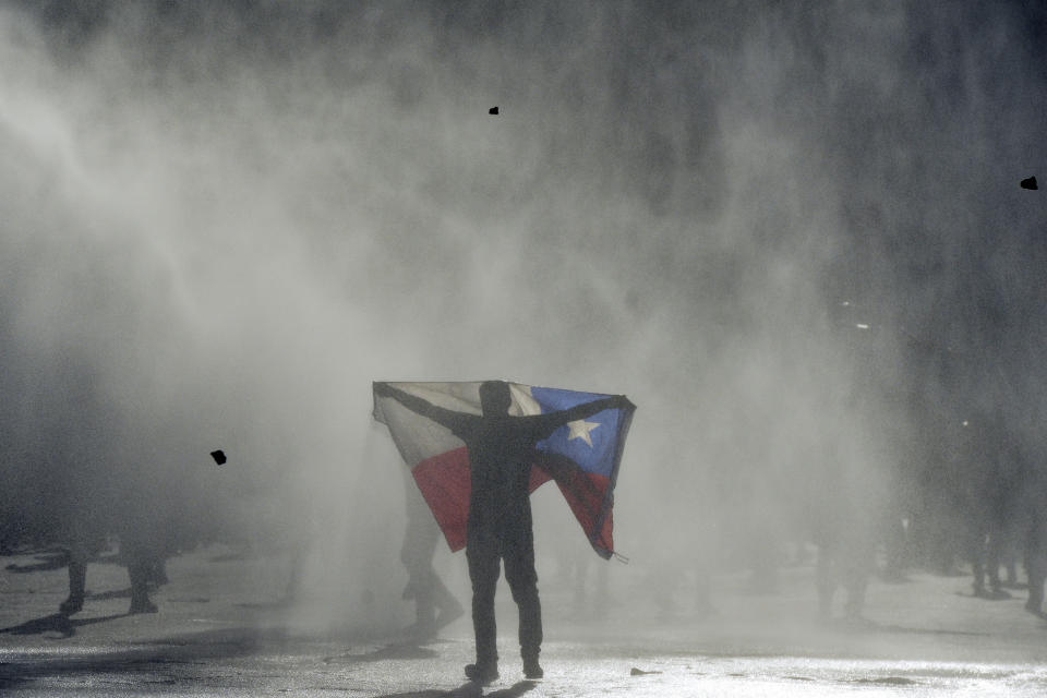 An anti-government protester holds out Chilean flag during clashes with police in Valparaiso, Chile, Friday, Oct. 25, 2019. A new round of clashes broke out Friday as demonstrators returned to the streets, dissatisfied with economic concessions announced by the government in a bid to curb a week of deadly violence.(AP Photo/Matias Delacroix)