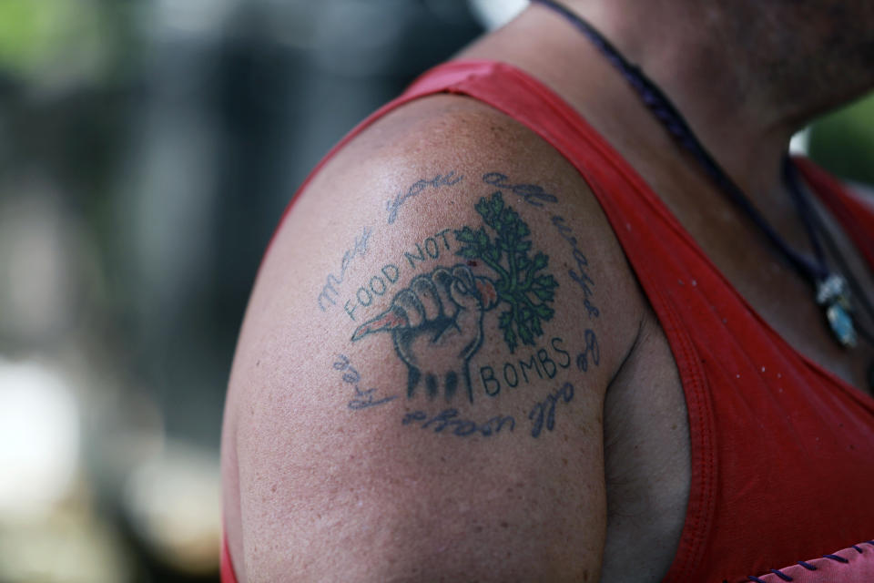 A tattoo reading "food not bombs" seen on the shoulder of a chef cooking in a kitchen at the annual Rainbow gathering on Friday, July 2, 2021, in the Carson National Forest, outside of Taos, N.M. More than 2,000 people have made the trek into the mountains of northern New Mexico as part of an annual counterculture gathering of the so-called Rainbow Family. While past congregations on national forest lands elsewhere have drawn as many as 20,000 people, this year’s festival appears to be more reserved. Members (AP Photo/Cedar Attanasio)