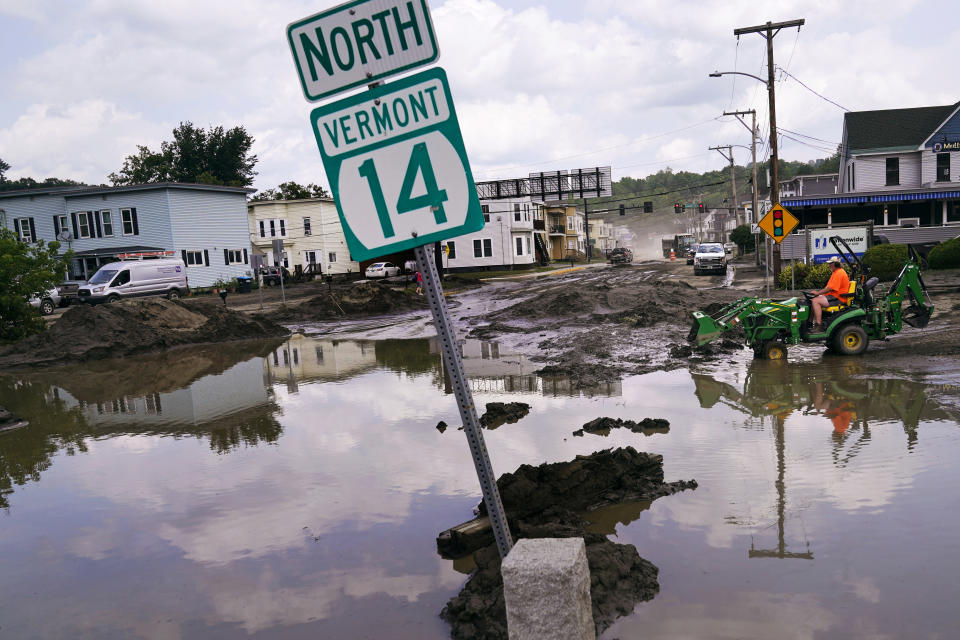 FILE - A small tractor clears water from a business as flood waters block a street, July 12, 2023, in Barre, Vt. The Vermont legislature is advancing a bill that would require fossil fuel producers to pay for some of the state's recovery costs from climate-related storms. (AP Photo/Charles Krupa, File)