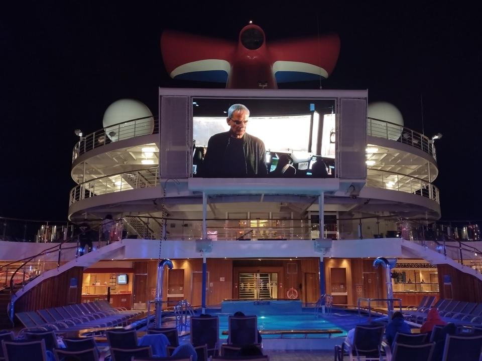 Mega TV screen playing a movie above a pool at night on Carnival Radiance cruise ship