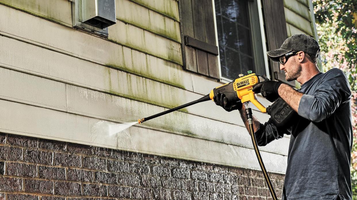  Man cleans vinyl siding with cordless dewalt pressure washer. 