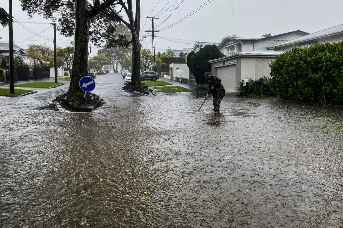 A man attempts to clear a drain in a flooded street in central Auckland, New Zealand (AP)