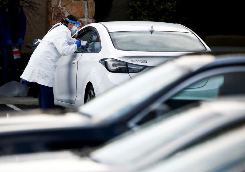 A nurse administers a nasal swab through a car window outside Life Care Center of Kirkland