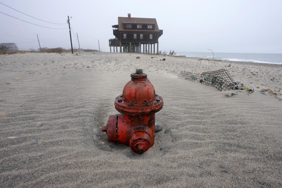 A half-buried fire hydrant rests near a house on pylons on the beach, Thursday, Jan. 25, 2024, in South Kingstown, R.I. Experts say erosion and receding shorelines are becoming more common due to ocean rise and climate change. (AP Photo/Steven Senne)